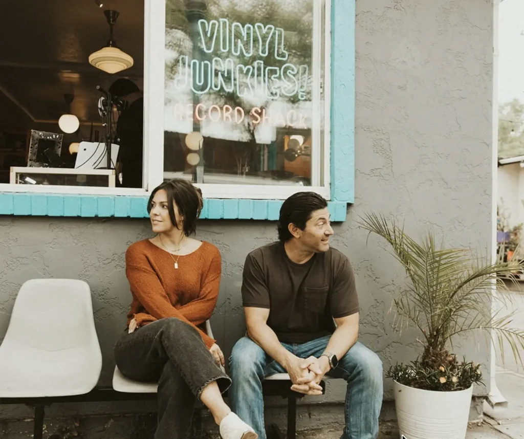 Two people sitting together in a modern cafe or creative studio with plants and a warm interior.